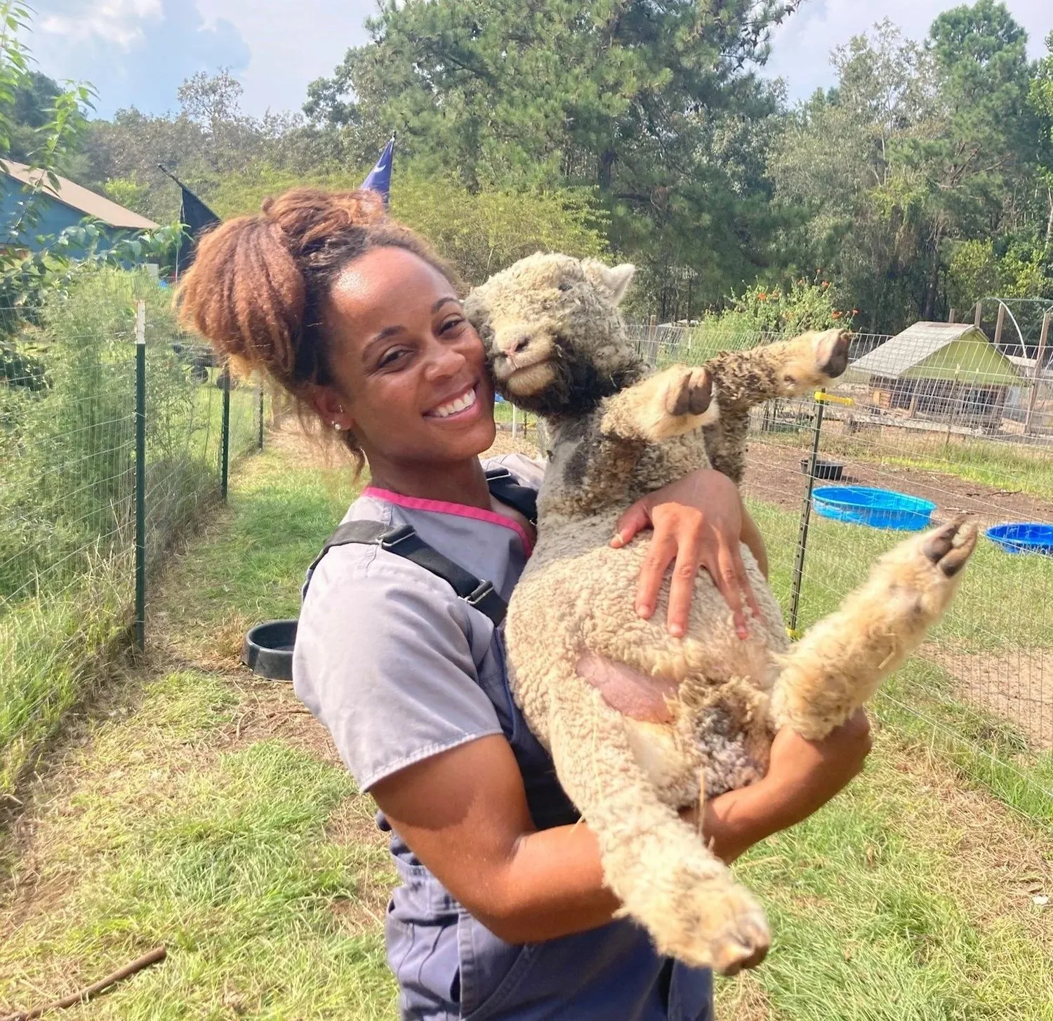 An Ark veterinarian smiling while holding an alpaca on a farm